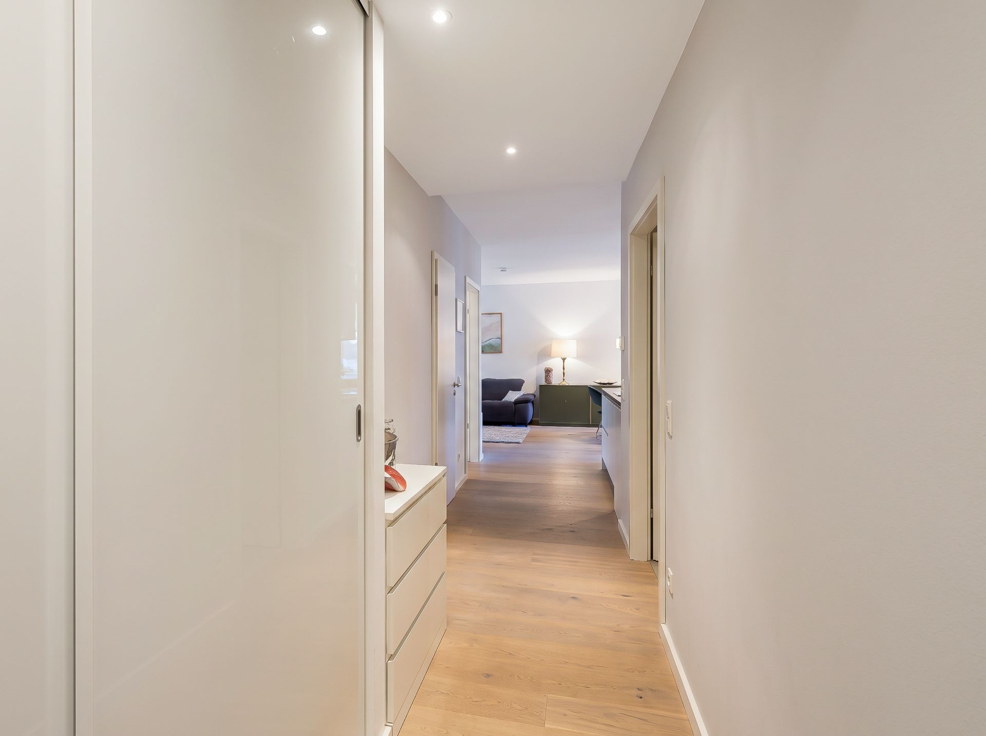 Heller Flur mit Holzfußboden und Sicht auf Wohnzimmer mit Sofa und Lampe.