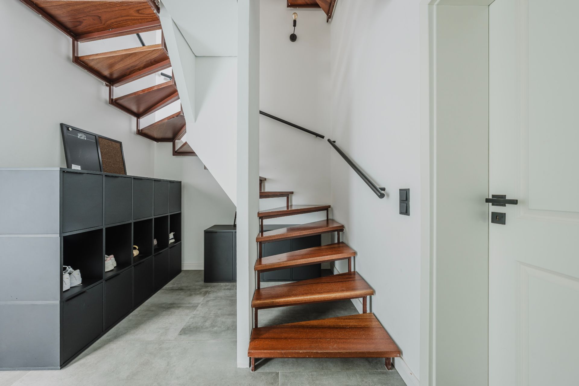 Moderne Holztreppe mit offenem Regal darunter in einem hellen Flur.