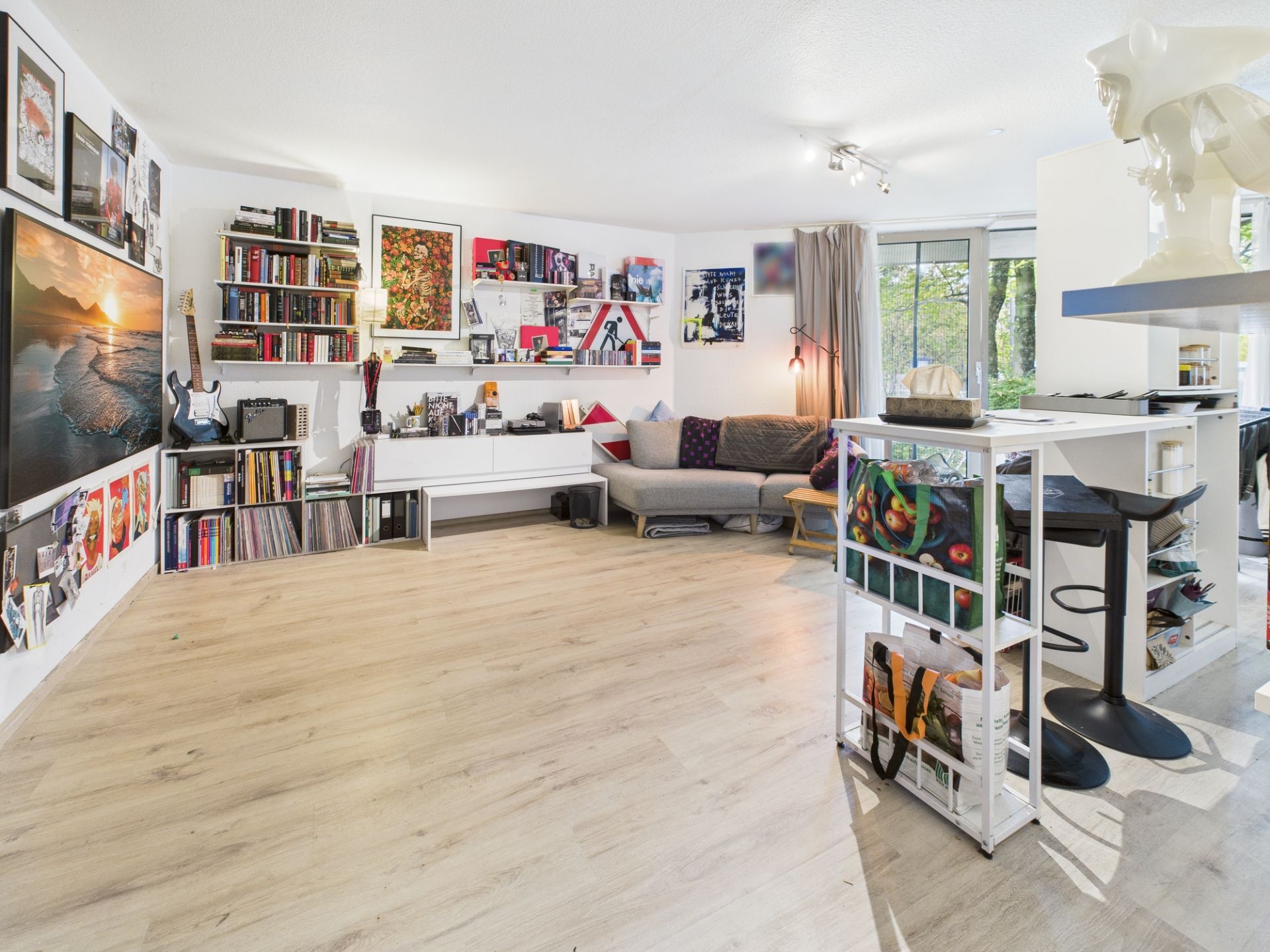 Helles Wohnzimmer mit Holzfußboden, Sofa, Bücherregalen und großer Fensterfront.