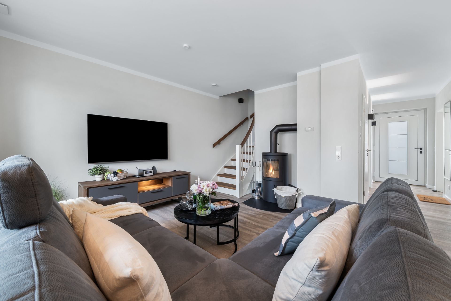 Modernes Wohnzimmer mit Ecksofa, Fernseher, Kaminofen und Treppe im Hintergrund.