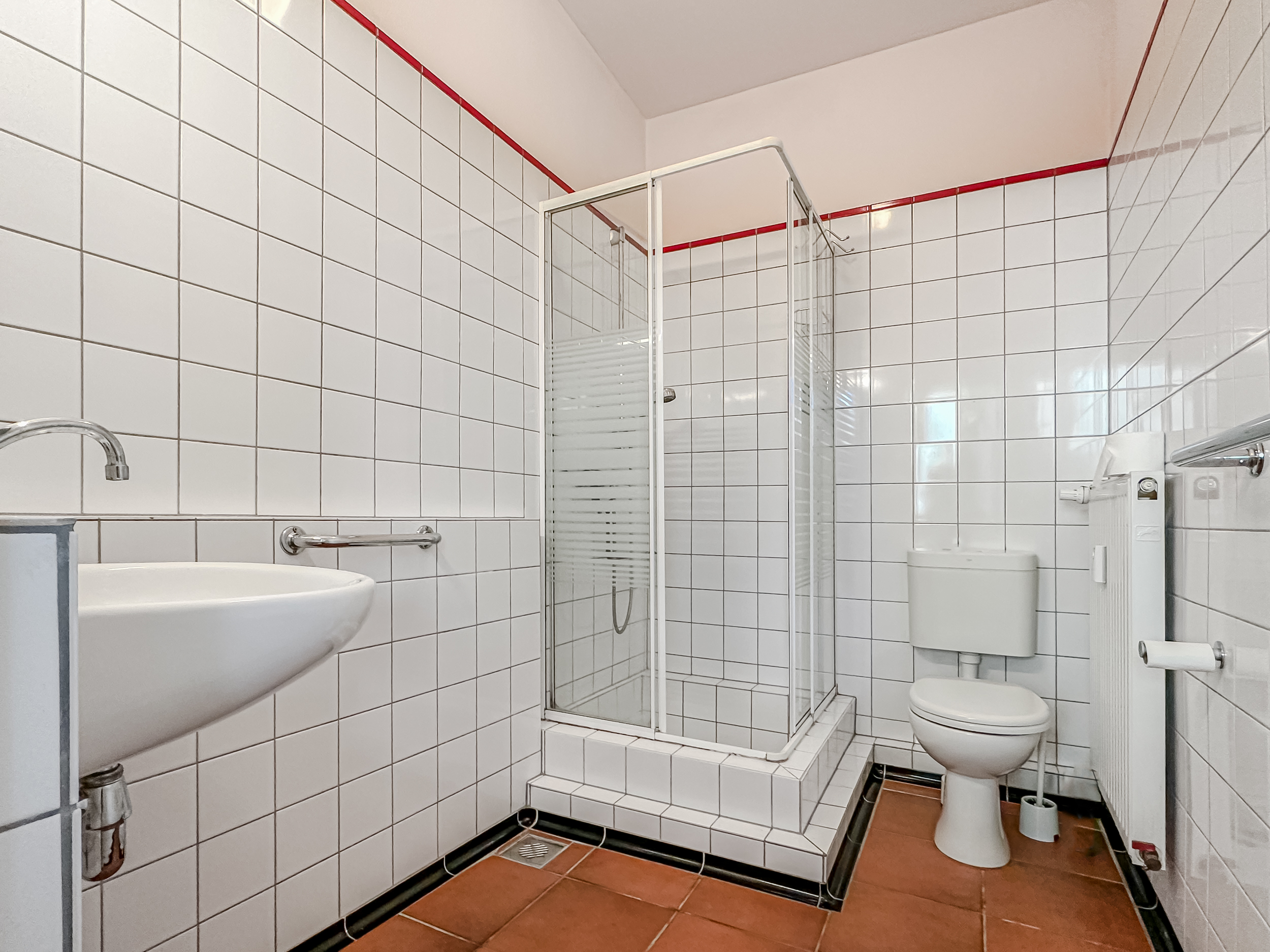Helles Badezimmer mit Dusche, WC, Waschbecken und weißen Fliesen an den Wänden.