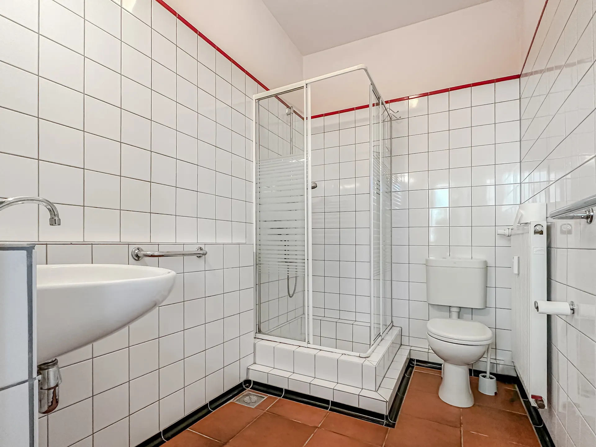 Helles Badezimmer mit Dusche, WC, Waschbecken und weißen Fliesen an den Wänden.
