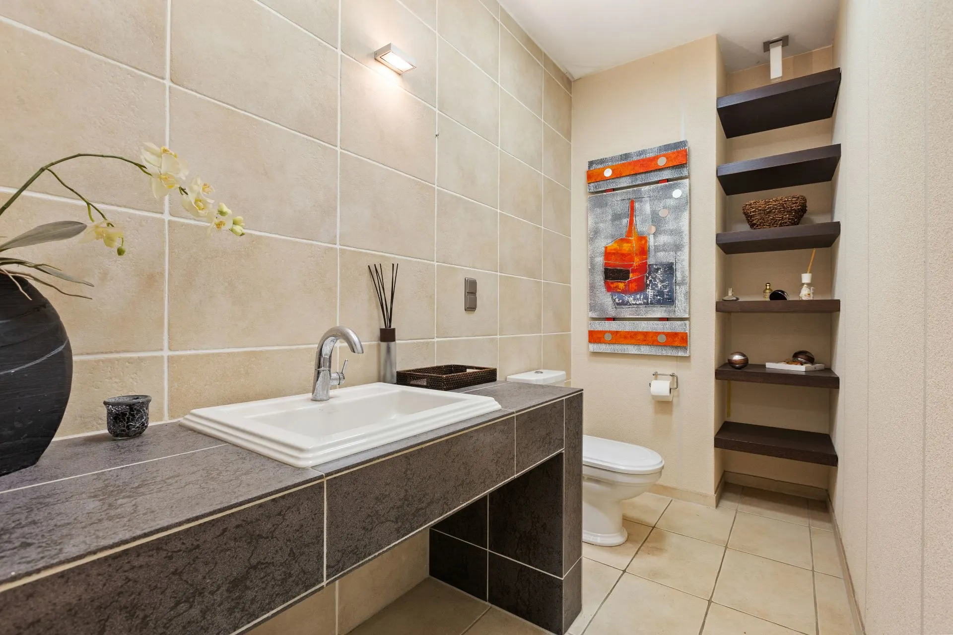 Modernes Badezimmer mit Waschbecken, Toilette, Kunstbild und offenen Regalen an der Wand.