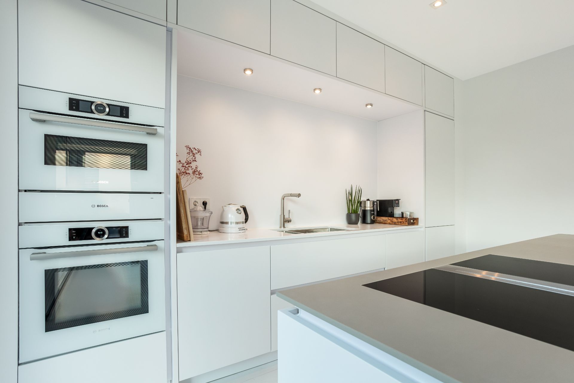 Moderne weiße Einbauküche mit Herd, Spüle, Backofen und Küchenutensilien.