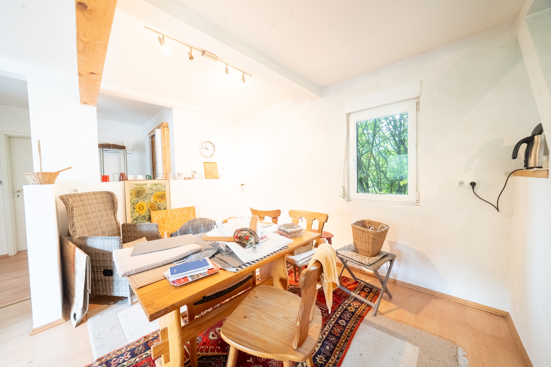 Helles Esszimmer mit Holztisch, Stühlen, Sessel, Fenster und Teppich auf dem Boden.