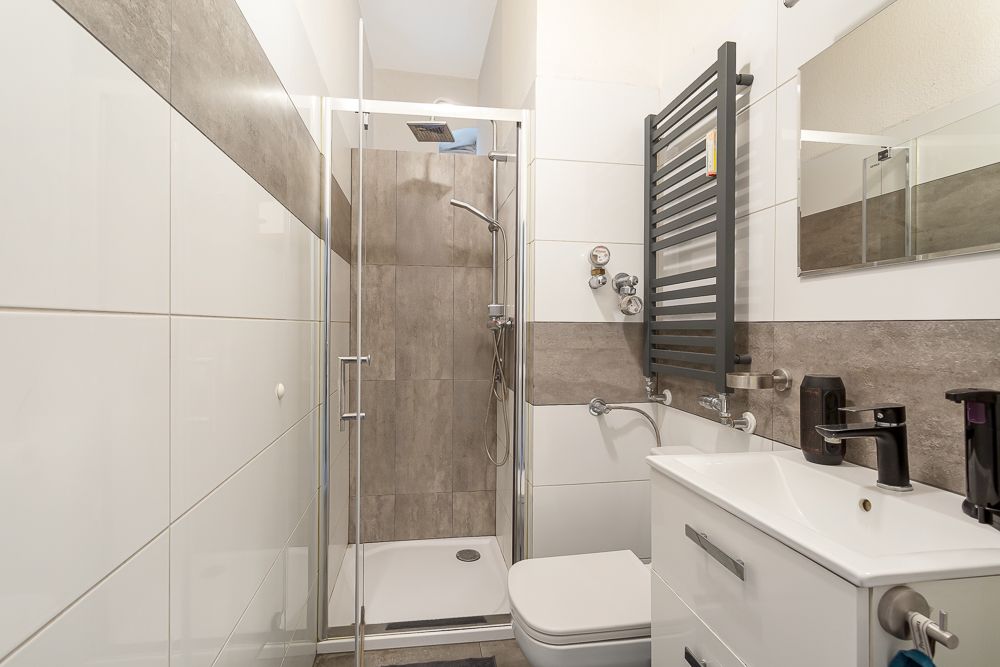 Modernes Badezimmer mit Dusche, Waschbecken, Toilette, Handtuchheizung und Fliesen.