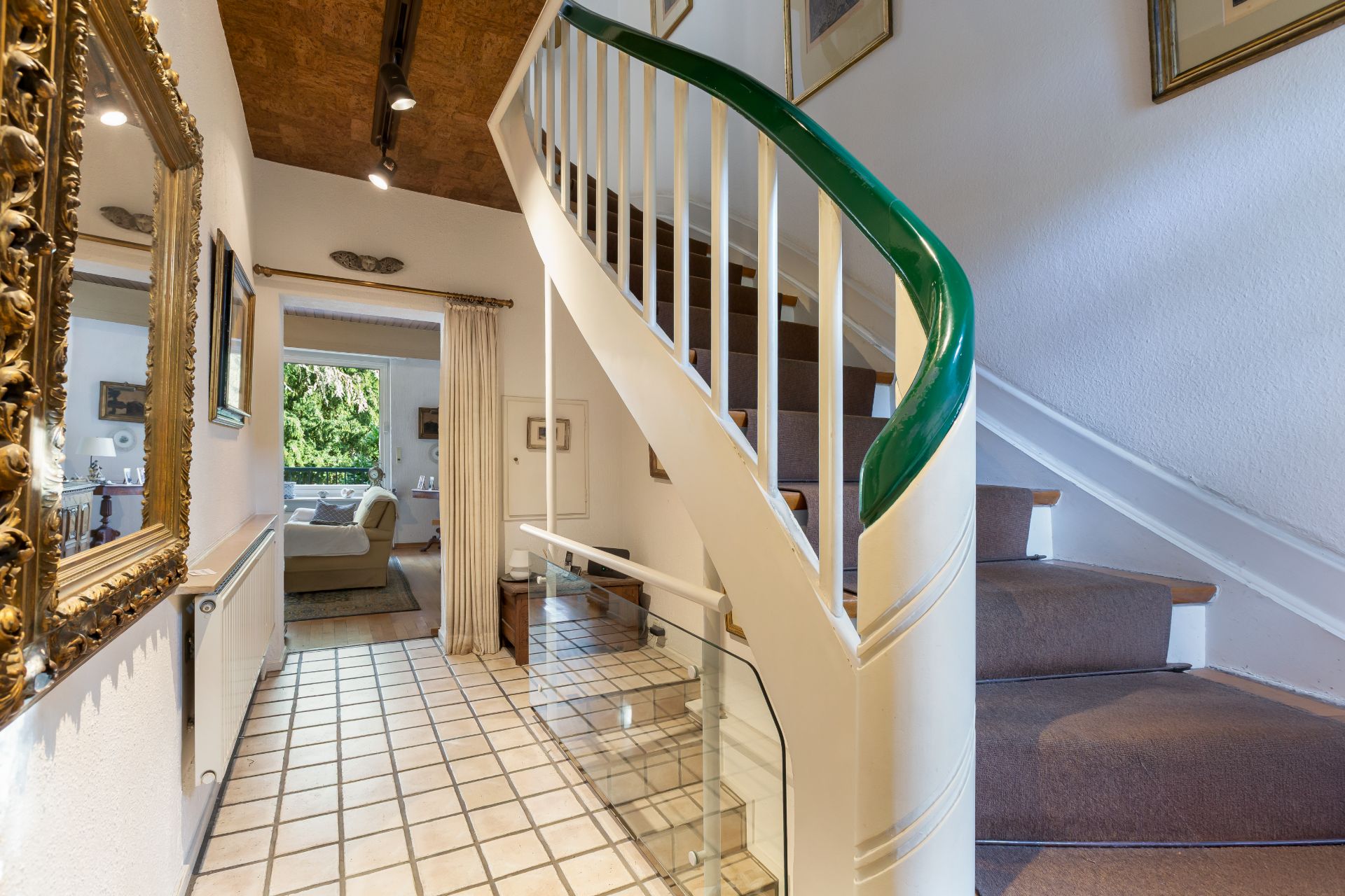 Helle Diele mit Fliesenboden, Spiegel, Treppe und Blick ins Wohnzimmer.