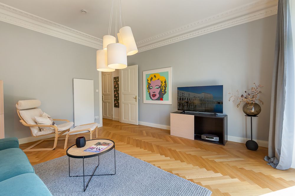 Helles Wohnzimmer mit Sessel, Sofa, Couchtisch, TV, Kunstbild und großem Fenster.