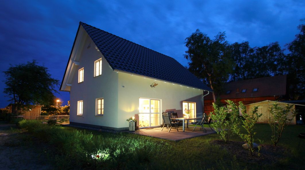 Zweistöckiges Haus mit beleuchteten Fenstern und Terrasse bei Nacht, umgeben von Garten.