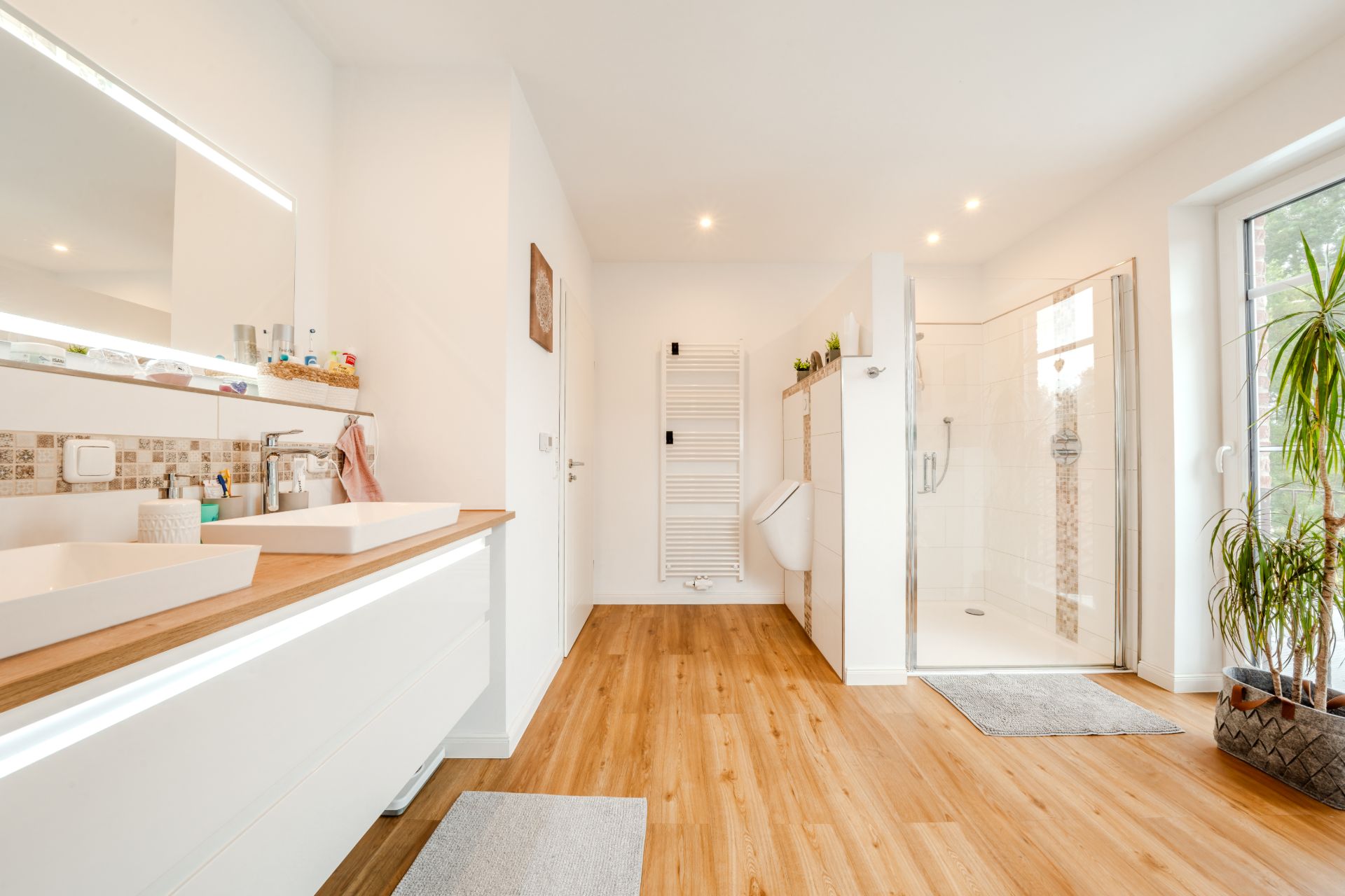 Modernes Badezimmer mit Doppelwaschbecken, Holzfußboden, Dusche und Pflanzen am Fenster.