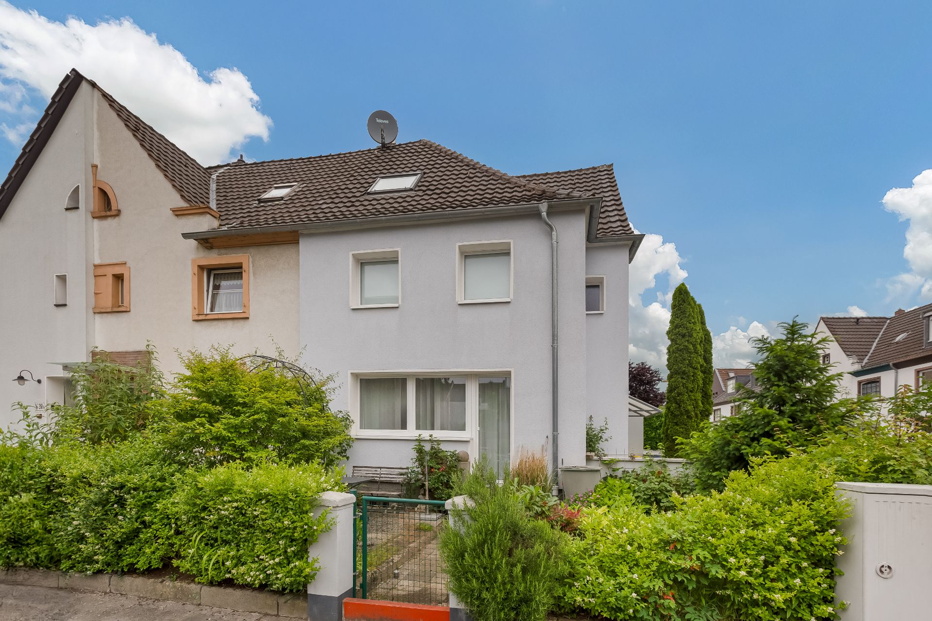 Zweistöckiges Wohnhaus mit Garten und grauem Zaun, umgeben von viel Grün.