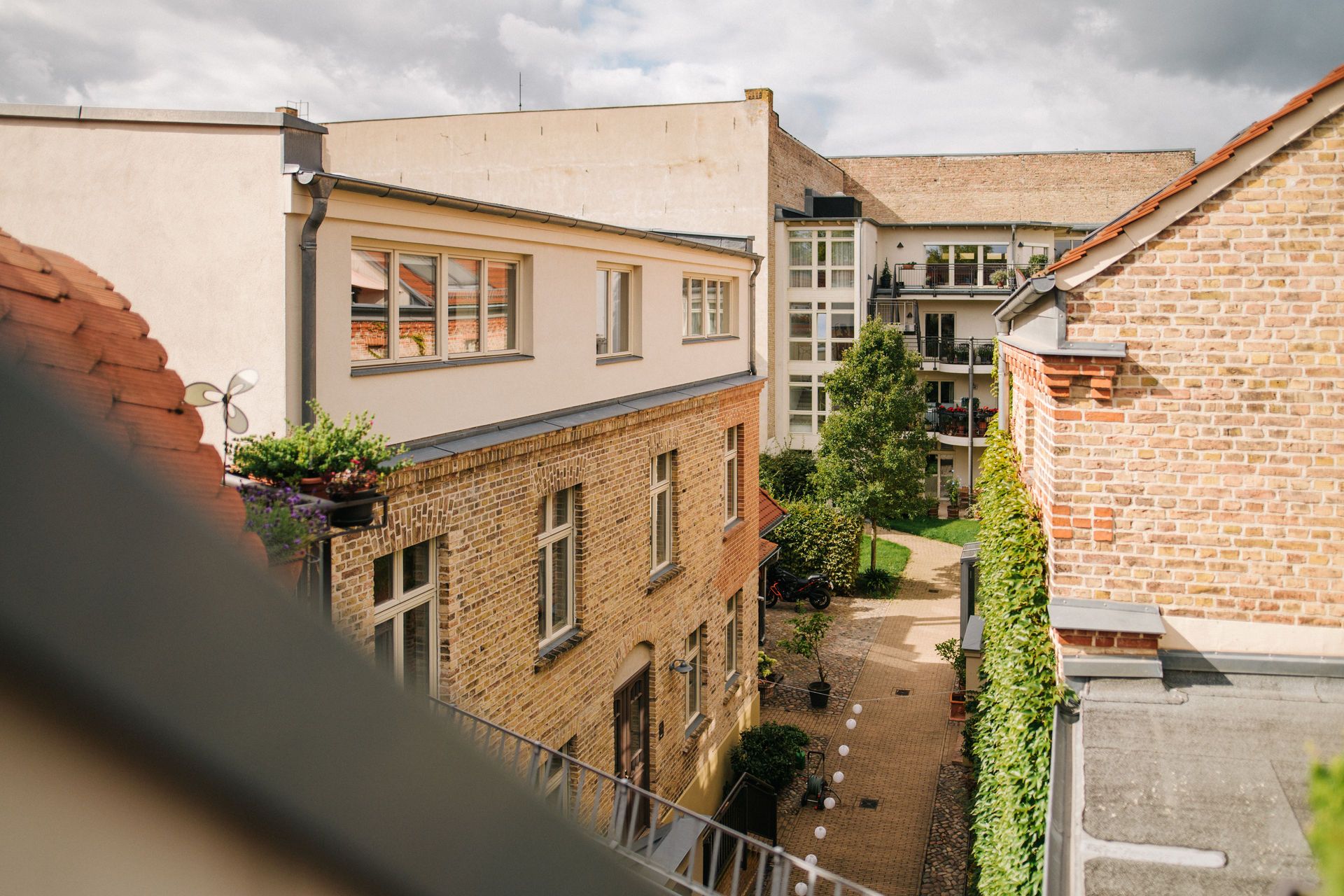 Blick auf einen Innenhof mit Backsteingebäuden, Bäumen und einem gepflasterten Weg.