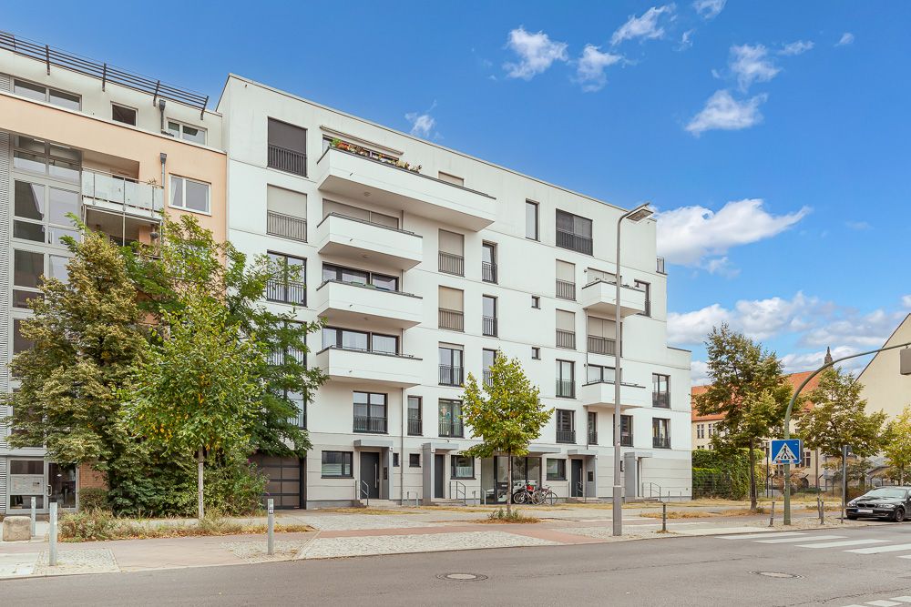 Modernes Wohnhaus mit mehreren Balkonen und Bäumen davor, an einer Straße gelegen.