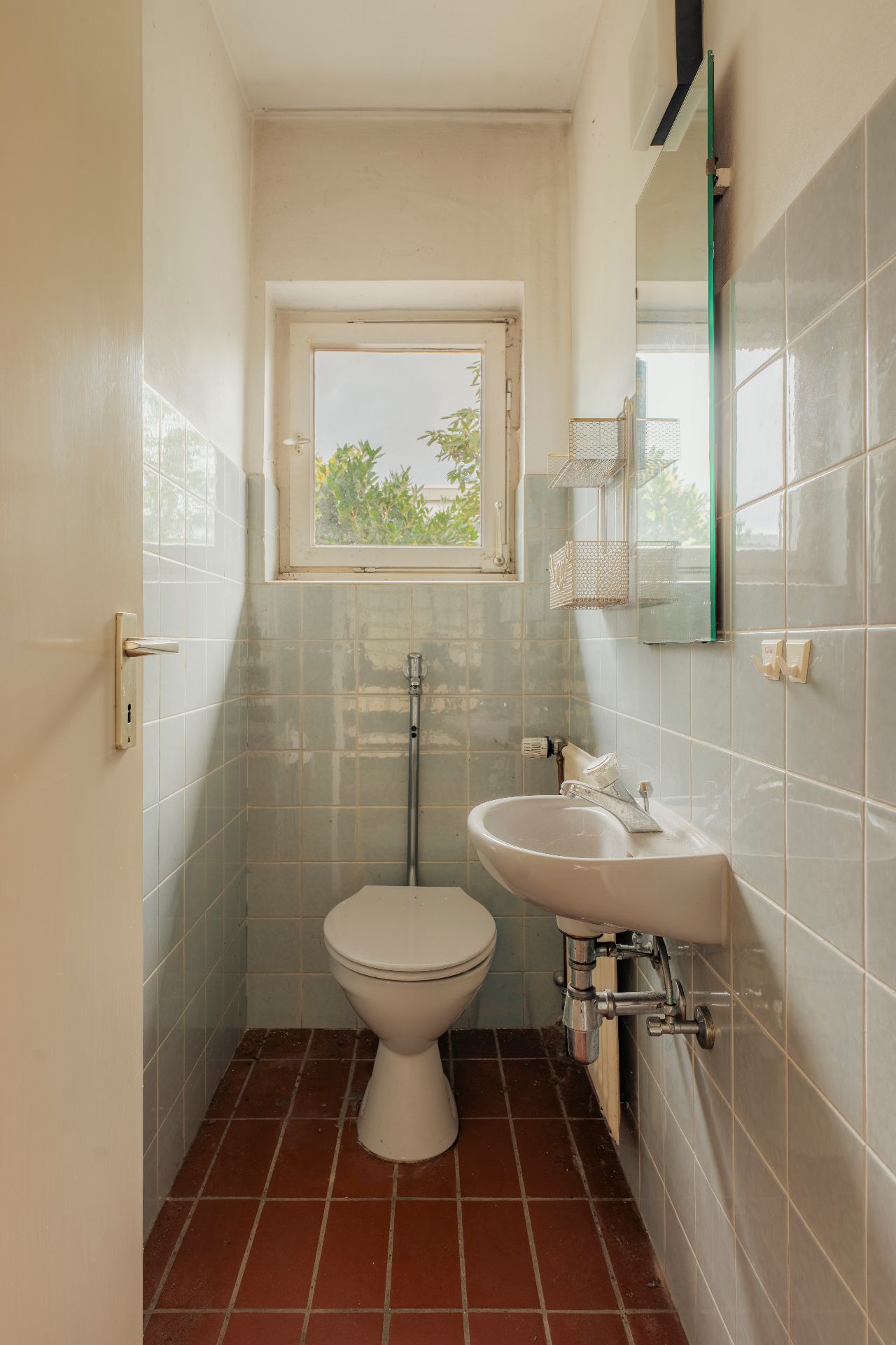 Kleines Bad mit Toilette, Waschbecken, Fenster und hellen Wandfliesen.