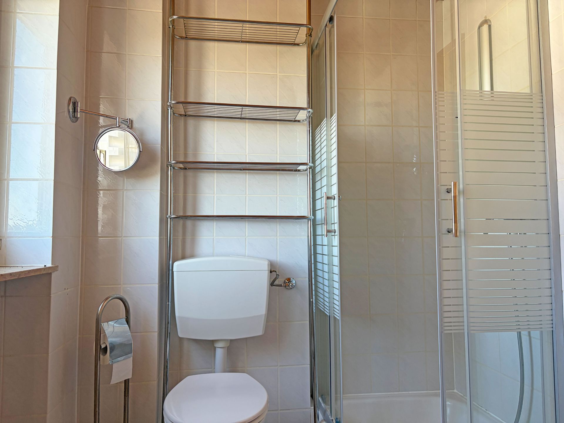 Kleines Badezimmer mit WC, Dusche, Wandregal und kleinem Fenster.