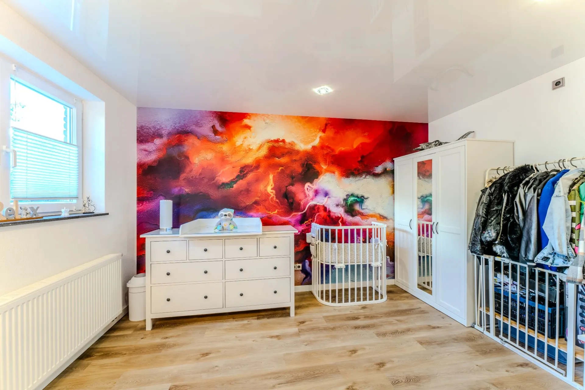 Kinderzimmer mit bunter Wandmalerei, Wickelkommode, Babybett und Kleiderschrank.