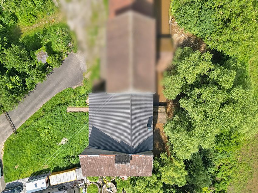 Luftaufnahme eines Hauses mit grauem Dach, umgeben von Bäumen und einer Zufahrtsstraße.