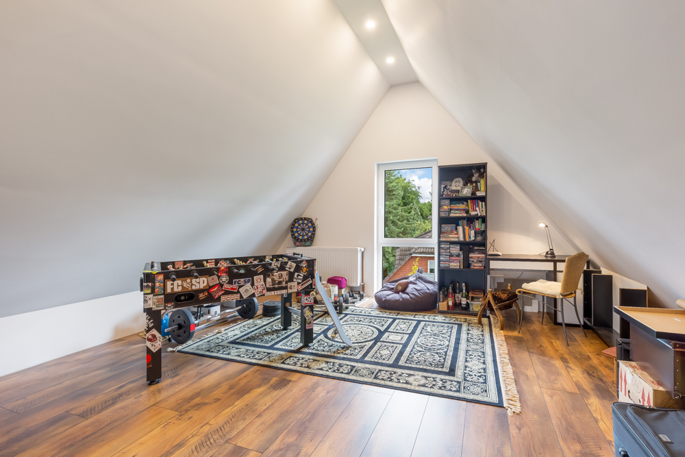 Zimmer mit schrägen Wänden, Kicker, Teppich, Bücherregal, Schreibtisch und Sitzsack.