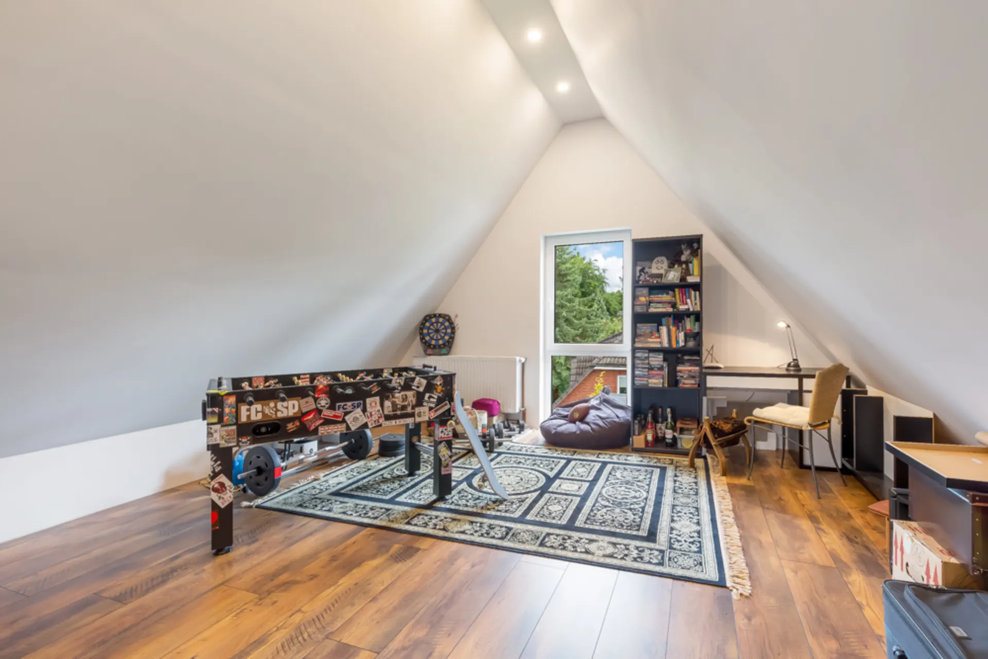 Zimmer mit schrägen Wänden, Kicker, Teppich, Bücherregal, Schreibtisch und Sitzsack.