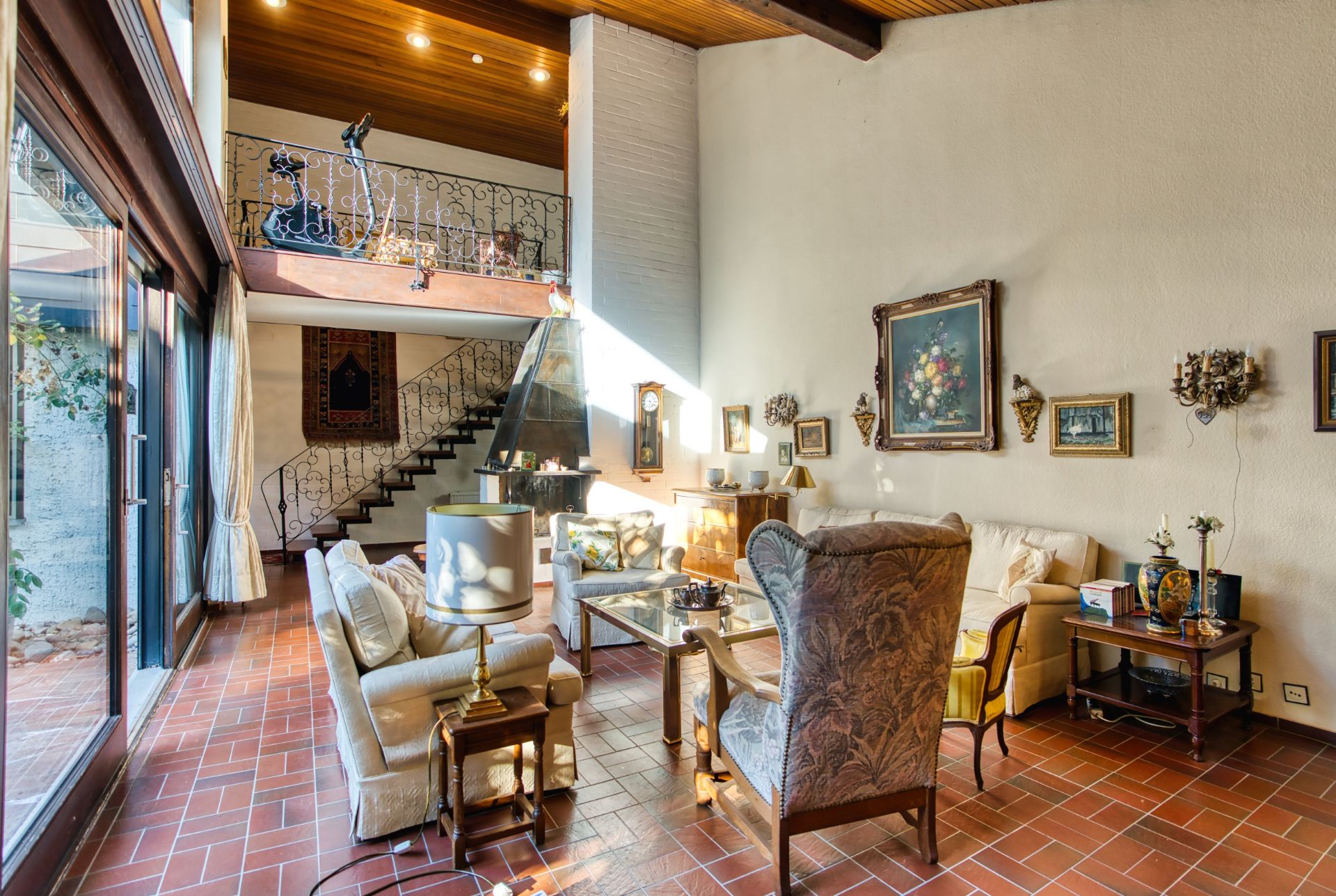 Helles Wohnzimmer mit hohen Decken, Sitzmöbeln, Treppe und Galerie, viele Wandbilder.
