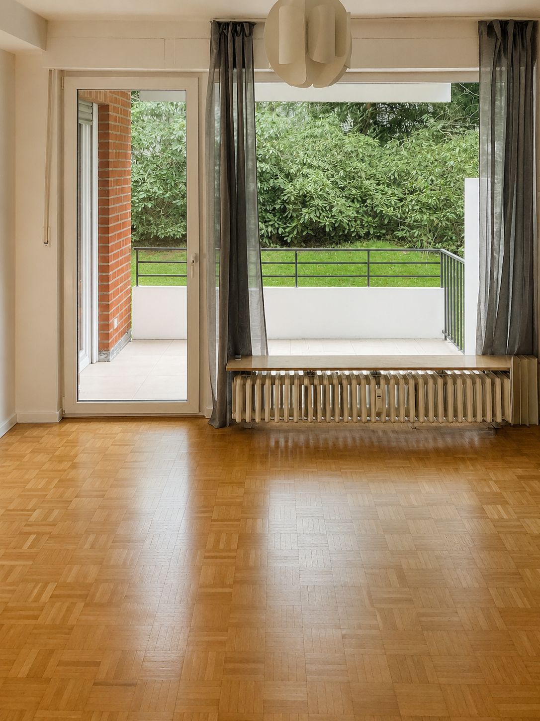 Helles Wohnzimmer mit Parkett, Heizung, Glasür und Zugang zum Balkon mit Blick ins Grüne.