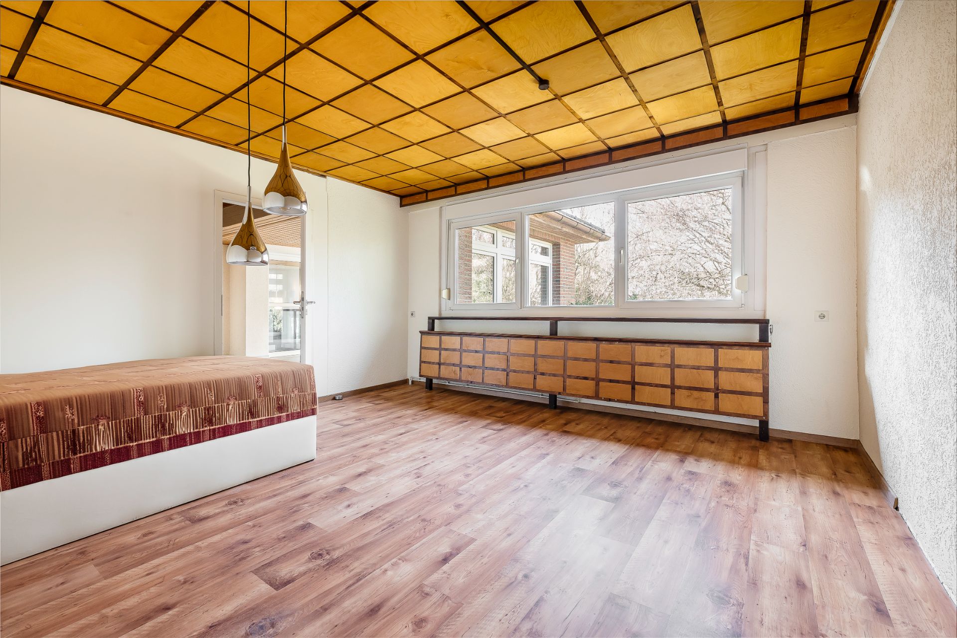 Helles Schlafzimmer mit Holzboden, großem Fenster, Bett und langer Kommode.