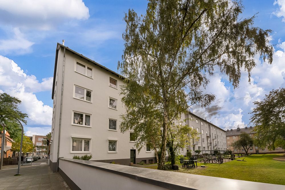 Wohngebäude mit mehreren Fenstern, Baum und Fahrrädern im begrünten Innenhof.