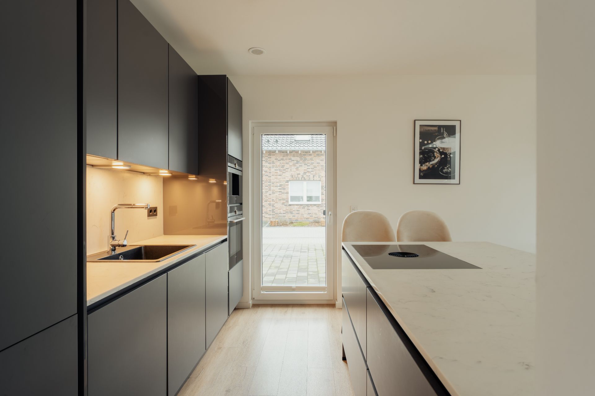 Moderne Küche mit dunklen Schränken, Kochinsel und großer Glastür zum Außenbereich.