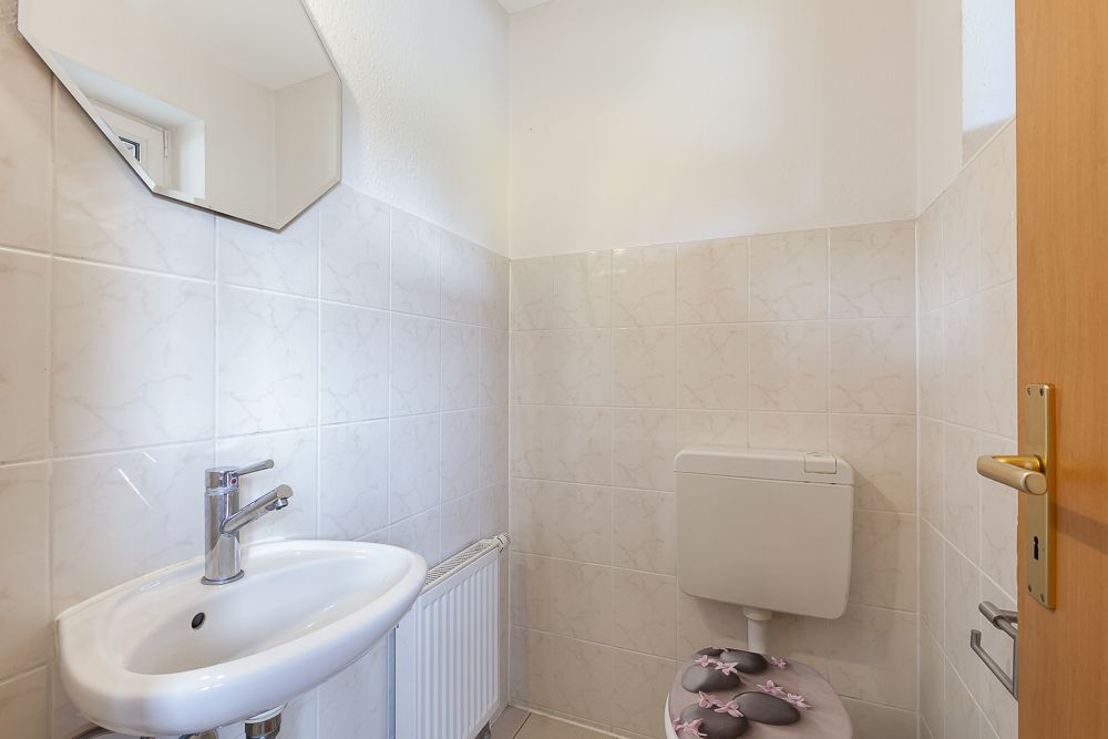 Kleines Badezimmer mit Waschbecken, Spiegel und Toilette mit mauerumgebenden Fliesen.