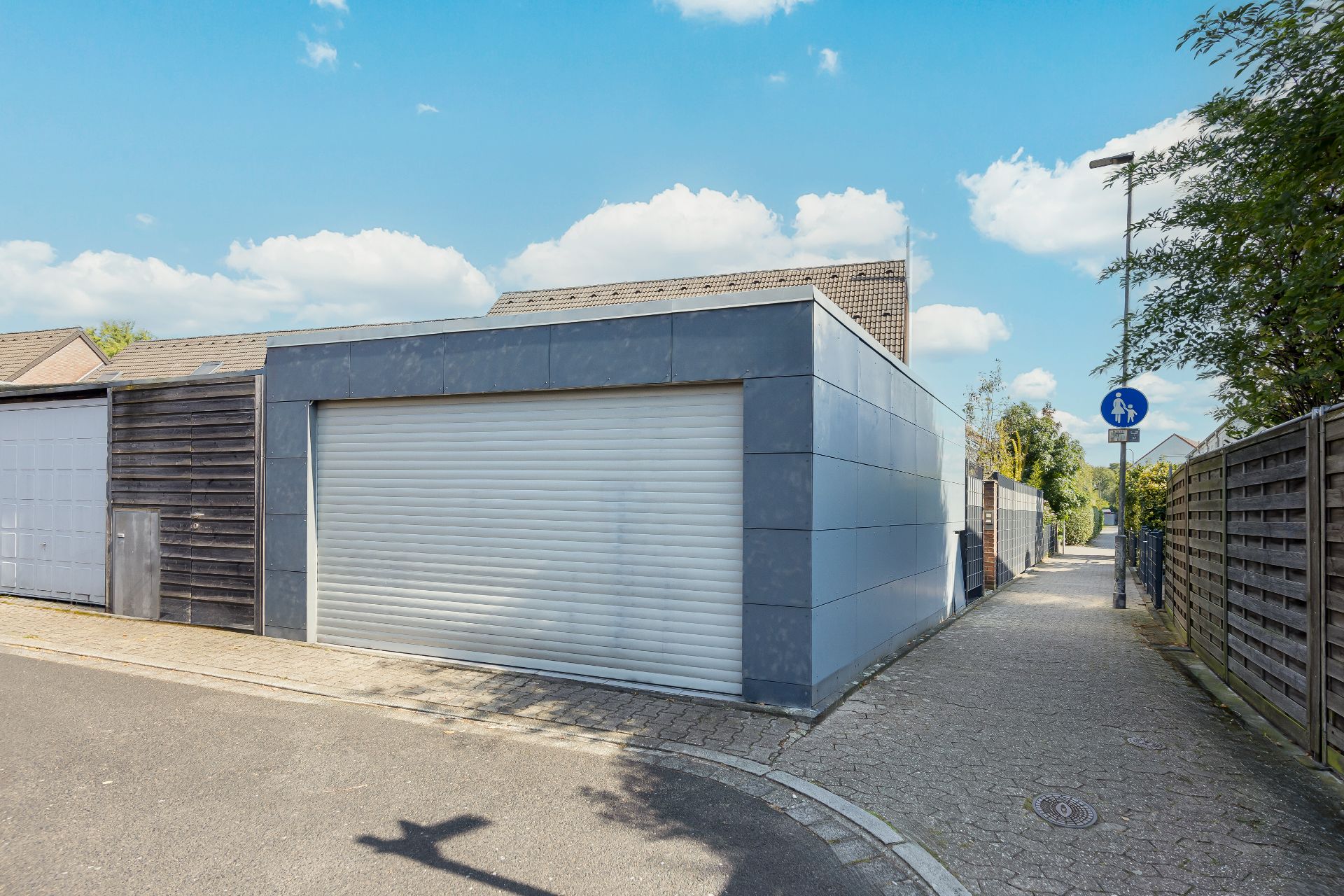 Garage mit geschlossenem Tor an einer Straße neben einem Gehweg bei sonnigem Wetter.