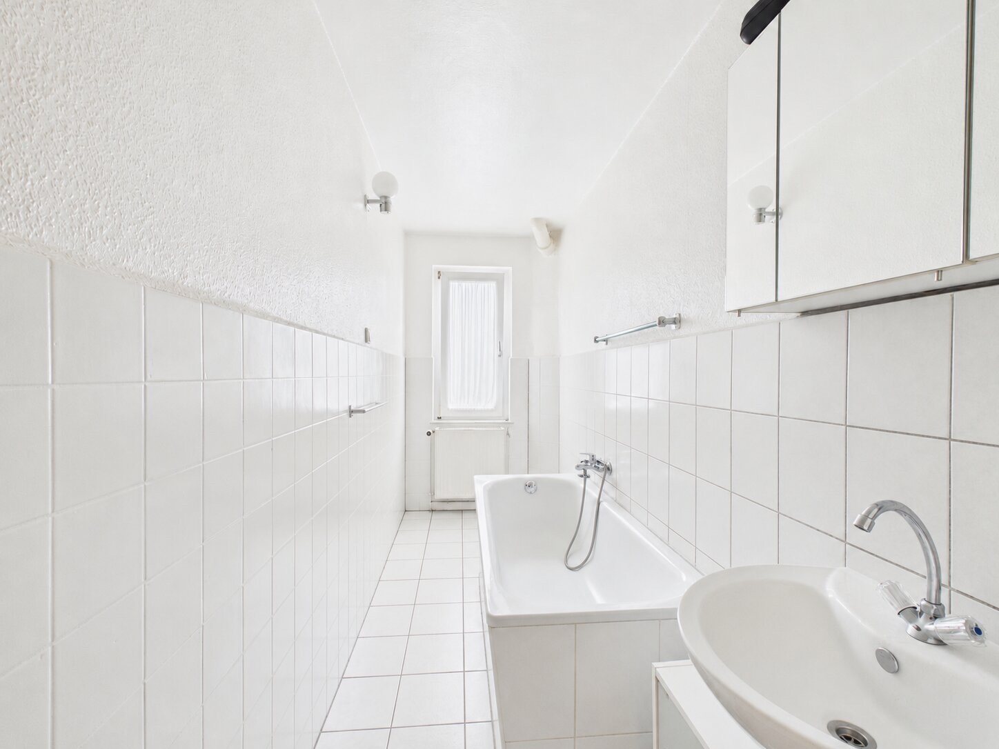 Helles Badezimmer mit Badewanne, Waschbecken, Spiegelschrank und Fenster.