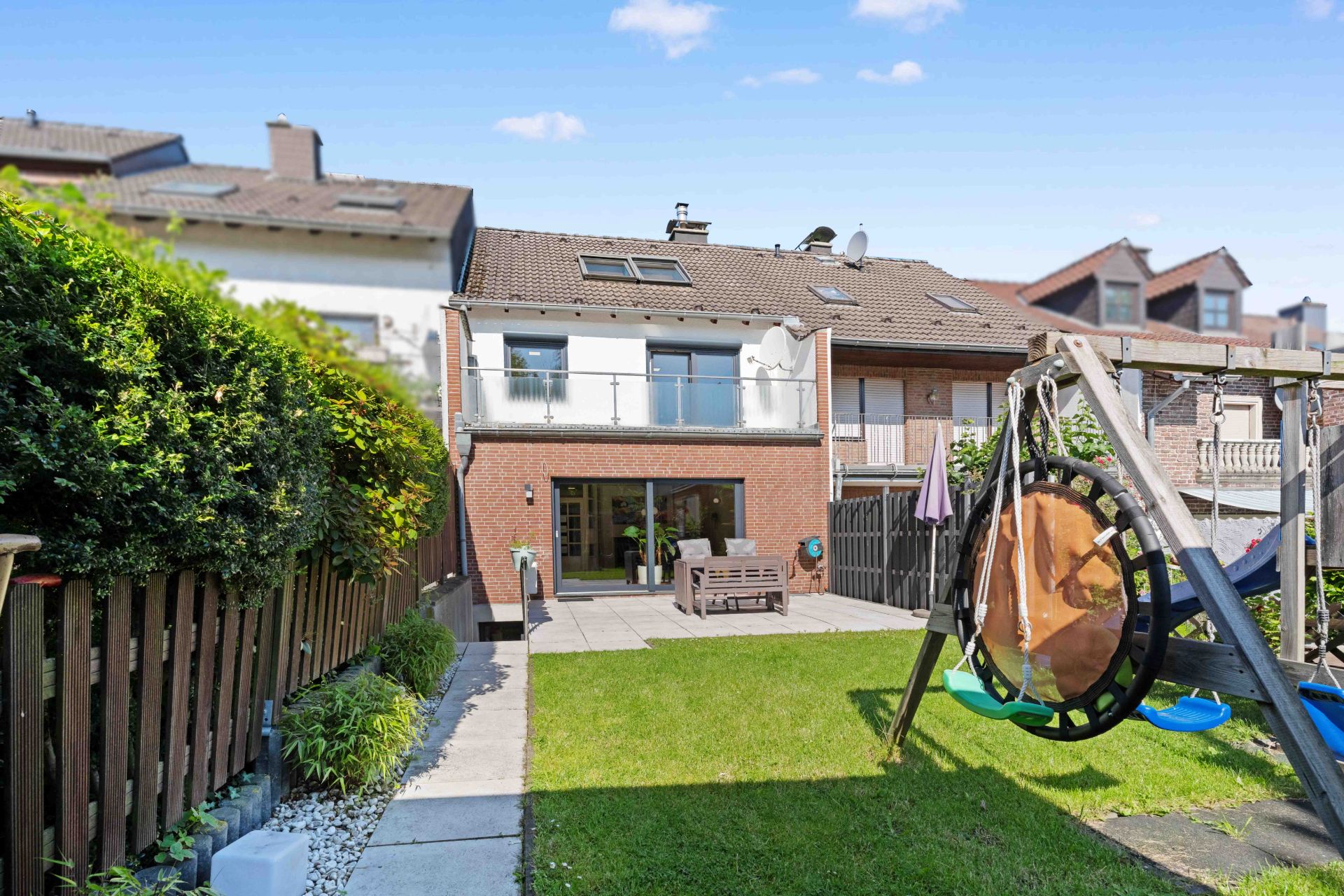Rückansicht eines Hauses mit Terrasse, Garten, Gartenmöbeln und Spielgerüst.