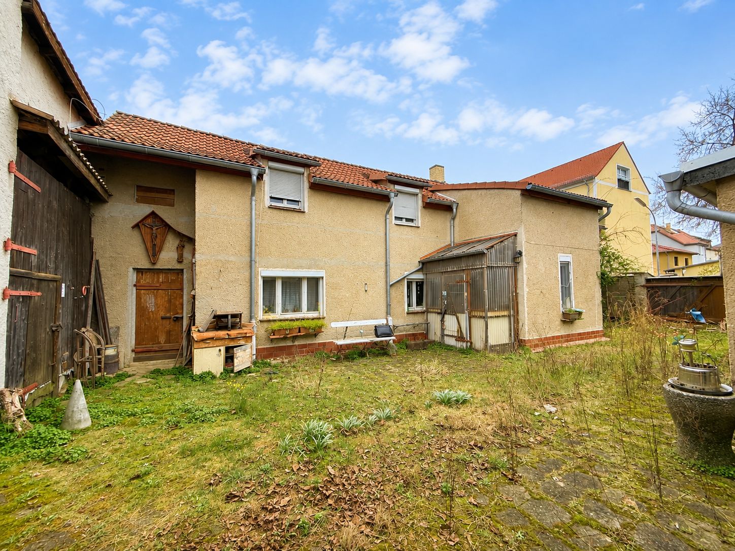 Hinterhof mit einem älteren Haus, Garten und einigen Pflanzen bei Tageslicht.