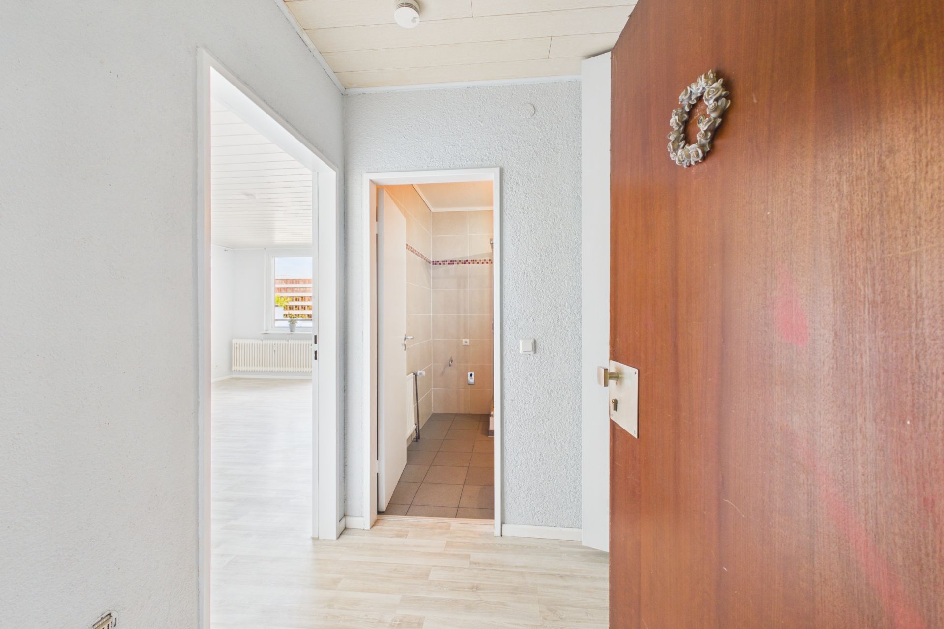 Blick in einen Flur mit geöffneter Holztür, Türen zu Bad und Wohnzimmer sichtbar.