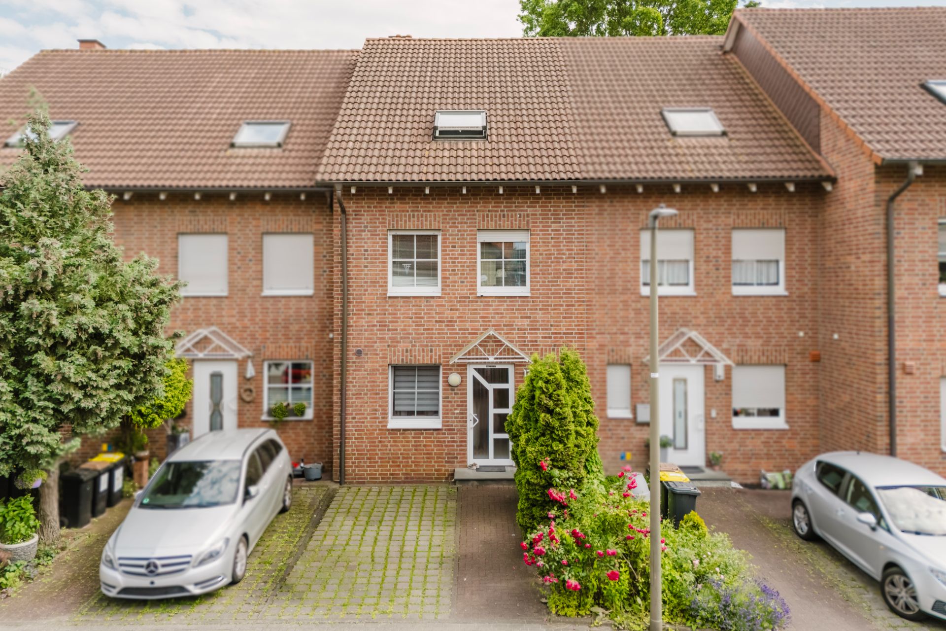 Reihenhaus aus rotem Backstein mit zwei geparkten Autos und Vorgarten.