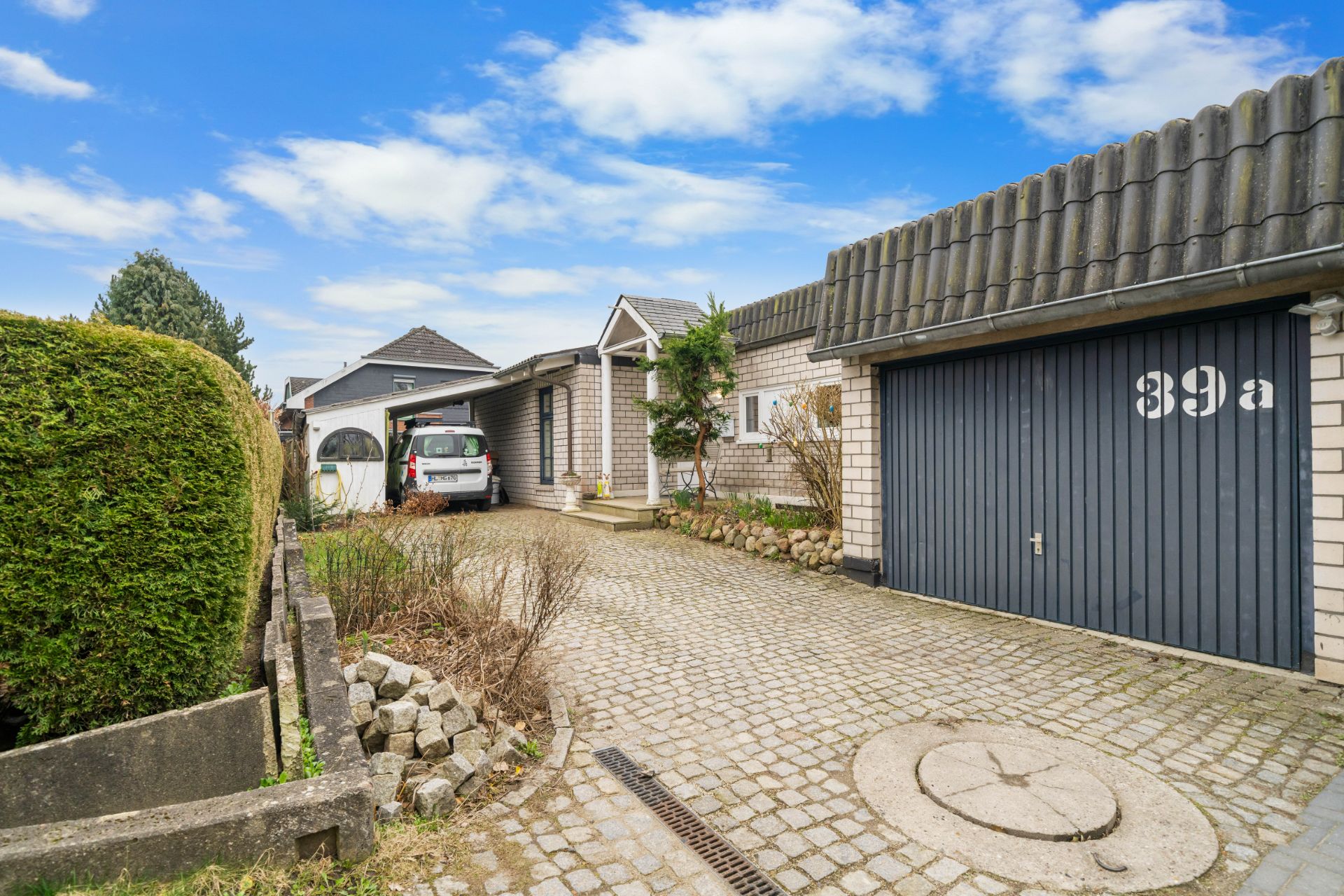 Gepflasterte Einfahrt mit freistehender Garage, Auto und Büschen an einem Wohnhaus.