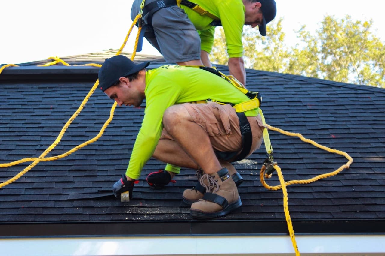 Two men from Taj Roofing are repairing the broken shingles of the roof