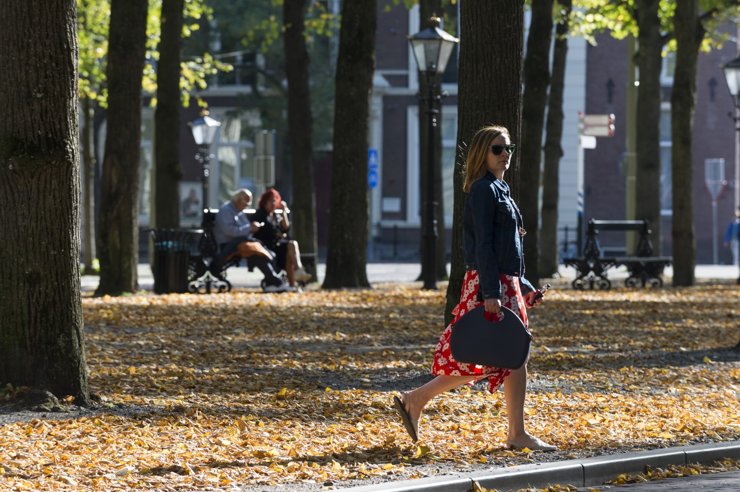 a woman walking down a leaf covered sidewalk