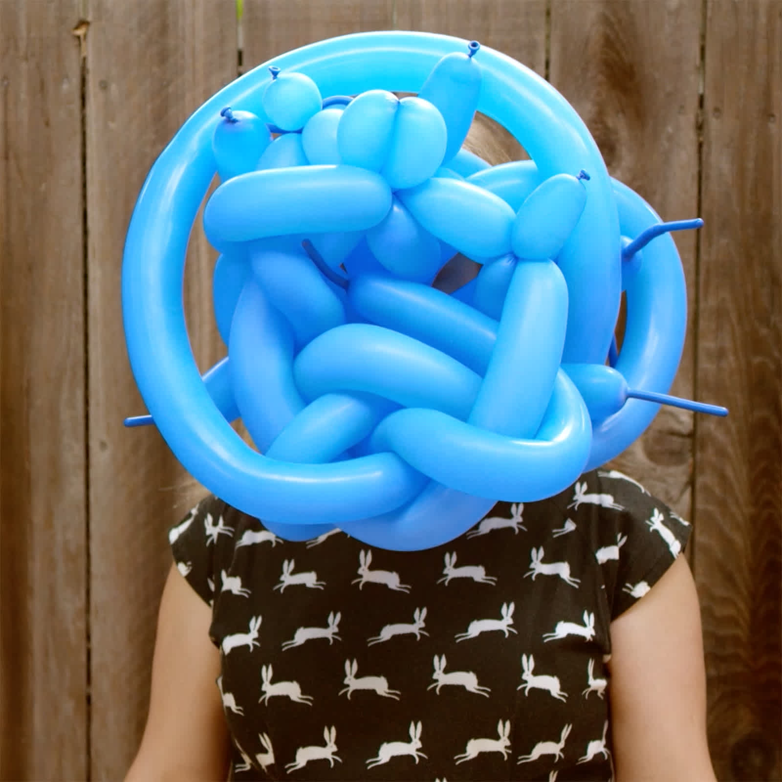 A woman wearing a dress holding a blue balloon over her face.
