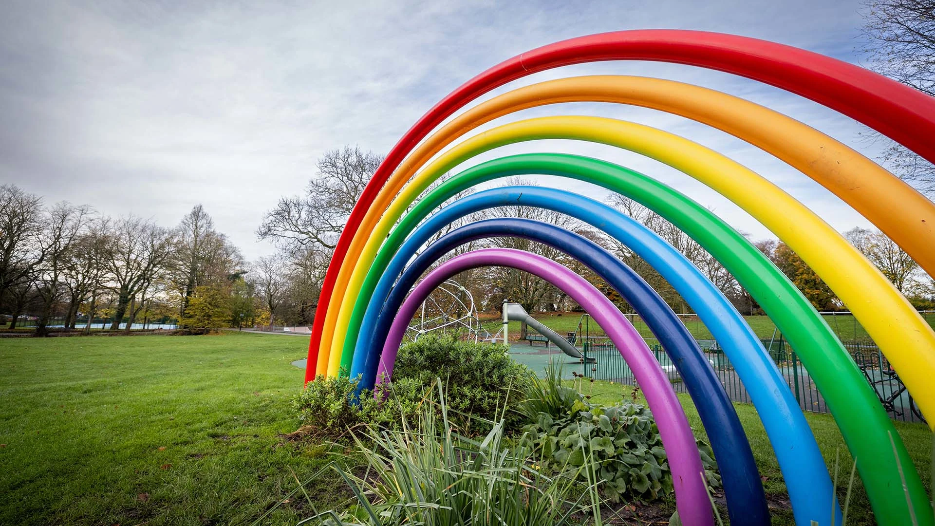 Bright rainbow sculpture, large brightly painted metal tubes to represent a rainbow with the playpark featuring a slide behind it