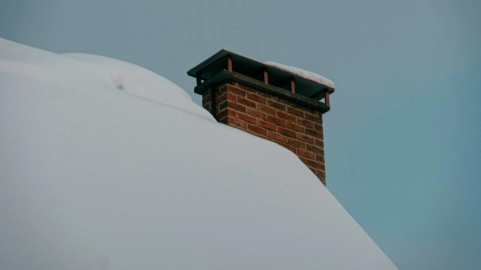 The roof of a house covered in snow. A brick chimney sticks out on the right.