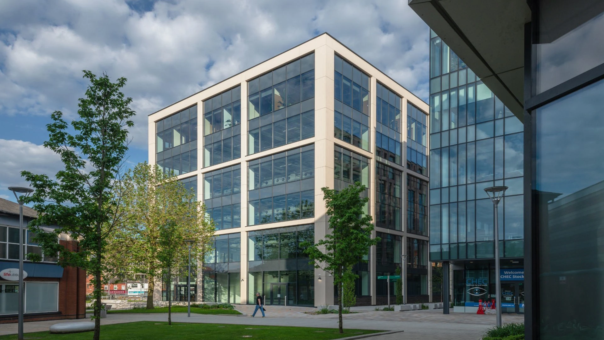 Modern glass office building with trees and a footpath in front.
