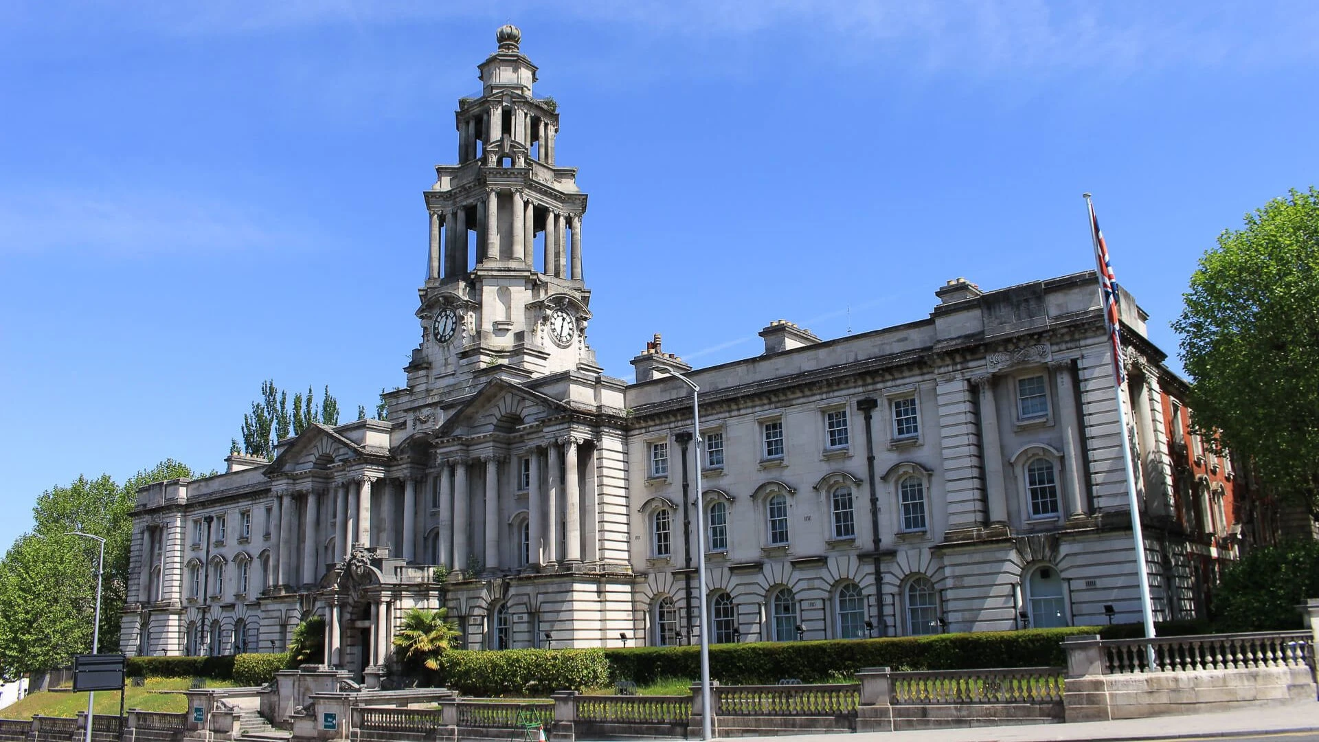 A large historic stone building with columns and a central clock tower under a clear blue sky.