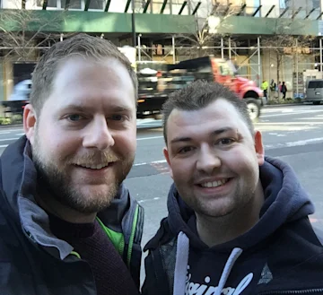 2 people smiling at the camera with buildings in the background
