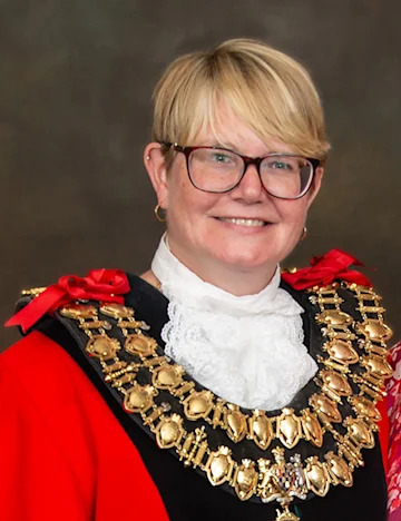 The Mayor, Councillor Kerry Waters stands and smiles at the camera. She is wearing a red cloak and large gold chains.