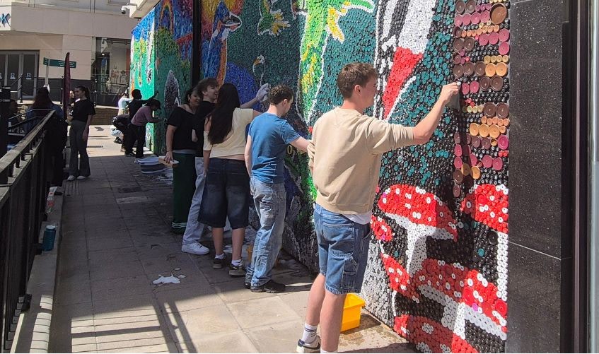A group of young people scrubbing the bottle-top mural outside Merseyway.