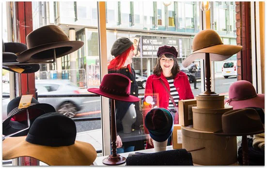 Two ladies looking at colourful hats in a shop window