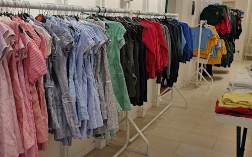 A clothing store display featuring neatly arranged children's school uniforms on metal clothing racks.
