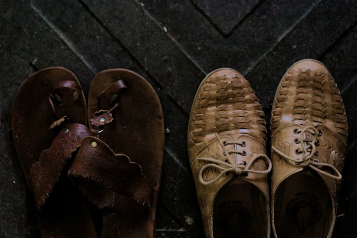 A pair of brown sandals on a black mat next to a pair of beige brogues.