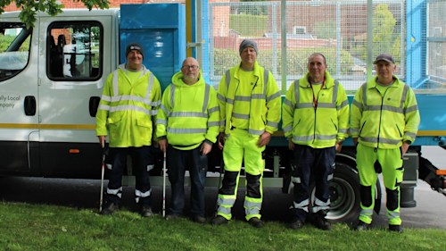 A group of TLC officers in hi-vis jackets standing with litter pickers outside a rubbish van.